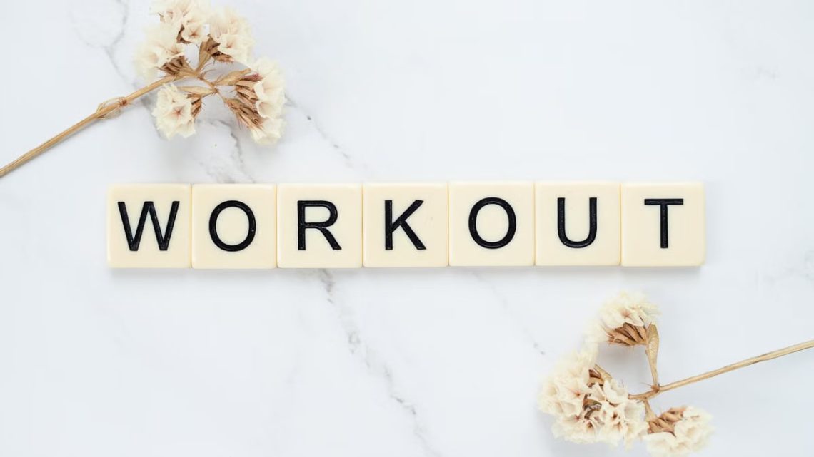 Letter tiles spelling 'WORKOUT' on marble with dried flowers, conveying fitness motivation.