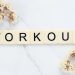 Letter tiles spelling 'WORKOUT' on marble with dried flowers, conveying fitness motivation.